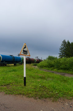 Road sign "Railway crossing without barrier" on the background of a train with oil tanks and a country road vertical orientation