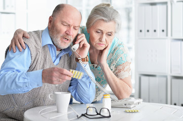 Portrait of ill senior couple at home calling doctor