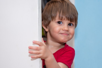 A little boy peeks out the door. The boy comes out of the pantry