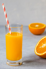 Tall glass of tasty freshly squeezed orange juice standing on table on hot summer day with halved fresh orange. Vertical layout