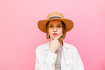 Pensive sad girl in light clothing and hat isolated on pastel pink background, looking into the camera at copy space and thinking. Pretty lady going through a pink background.