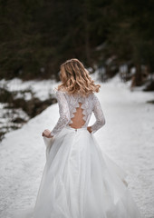 Fototapeta na wymiar bride with blonde hair running away from wedding in white traditional dress with open back during winter