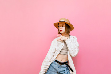 Pretty cheerful girl in light clothing and hat dancing on pink background. Attractive tourist girl dancing and looking aside, isolated on pastel pink background.Copy space