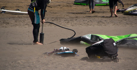 Alguien prepara su equipo de widsurf o kitesurf en una playa con mucho viento y un día soleado. Usando una bomba de aire.