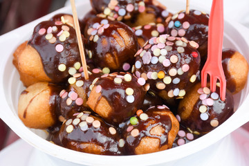 Fresh round small donuts during carnival or fast food festival, glazed with dark and white chocolate