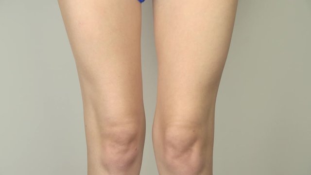 Sexy young woman puts on blue panties on a gray background. Legs close up