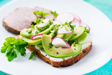 Tasty breakfast. Healthy avocado toast and radish on whole grain bread and baked sliced meat.