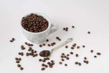 Fototapeta na wymiar Cup оf coffee , white ceramic cup with roasted coffee beans and a teaspoon on a white background. Isolate. Space for text.