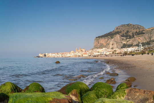 Idyllic view of Cefalu from the long sandy beach. Cathedral and Rocca di Cefalu rocky mountain on a sunny day in Cefalu, Sicily, Southern Italy.