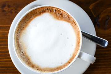 Simple coffee cup with milk foam on a white ceramic plate, on wooden background.