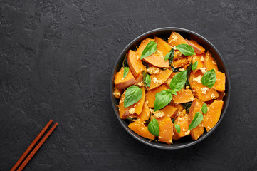 Pad Faktong or Thai Stir-fried Pumpkin in black bowl at dark slate backdrop. Pad Phuk Tong is thailand cuisine dish with sliced Kabocha Squash, eggs or tofu and basil. Thai Food. Top view. Copy space