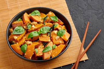 Pad Faktong or Thai Stir-fried Pumpkin in black bowl at dark slate background. Pad Phuk Tong is thailand cuisine dish with sliced Kabocha Squash, eggs or tofu and basil. Thai Food.