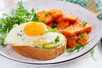 Healthy breakfast. Avocado sandwich with fried egg and fried sliced pumpkin with arugula for healthy breakfast or snack.