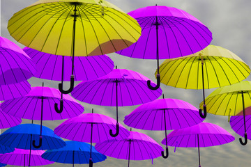 Fototapeta na wymiar Yellow and blue umbrellas against a cloudy sky. Colorful umbrellas background. Colorful umbrellas in the sky. Street decoration.