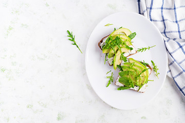 Sandwich of cream cheese bread and slices of avocado on a plate on a light background. Healthy vegetarian food. Top view, overhead, copy space