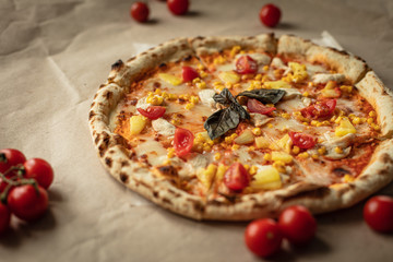 The pizza is big and round on the Kraft paper and wooden tray. Around the tomatoes and top view. The warm tones.