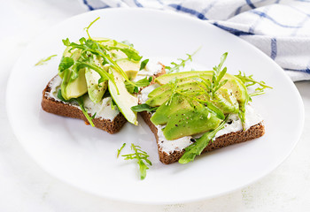 Sandwich of cream cheese bread and slices of avocado on a plate on a light background. Healthy vegetarian food.