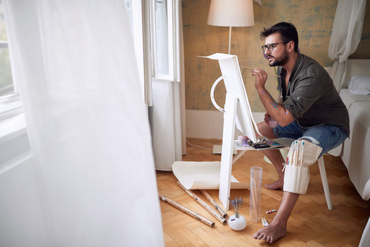 young male artist thoughtfully paint in a bedroom with white copy space of an curtain