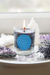 Obraz na płótnie Canvas Burning glass candle with homemade sign showing Flower of Life symbol in home interior with semi precious stone geodes. Spiritual symbols in home decor concept.