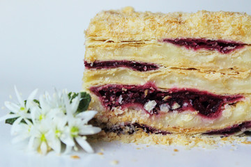 Piece of Napoleon cake with cherry jam decorating white flowers on the top. Food, dessert background.