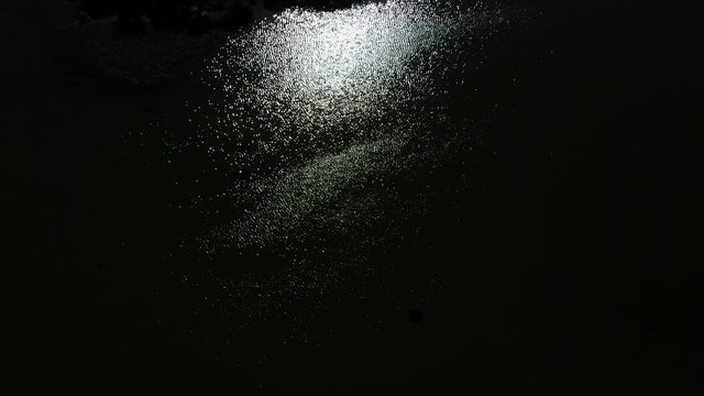 Vertical aerial view of sunlight sparkle on dark water surface as abstract nature background.