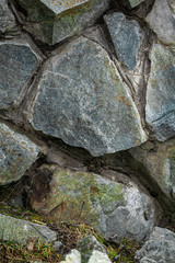 Several stones of different sizes and shapes on which moss grows are located next to grass.
