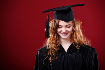 Portrait closeup. European beautiful smiley graduate graduated student girl young woman in cap gown on isolated red background wall. Celebrating graduation ceremony concept.