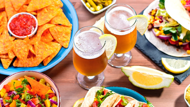 Table With Tacos, Mango Salsa, Nachos With Sauce, Guacamole, Lemon Beer. Appetizers And Traditional Mexican Dishes For Cinco De Mayo Or Taco Tuesday On Wooden Table Top, Copy Space