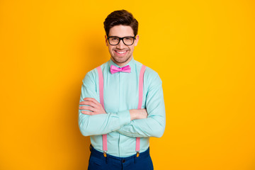 Photo of handsome cool clothes business guy stand self-confidently hands crossed beaming smile wear specs shirt suspenders bow tie trousers isolated yellow color background