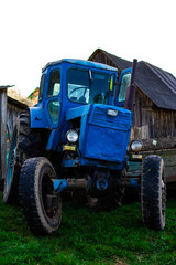 Old vintage blue rusty tractor on the background of farm buildings. Sowing work in the field.