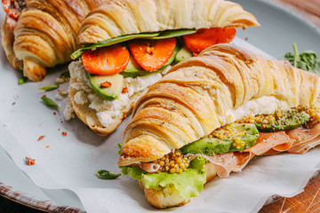 The concept of a hearty and tasty breakfast of fresh classic croissants with a variety of toppings from ricotta jamon avocado, strawberries, sun-dried tomatoes, and French mustard.