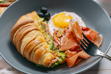 delicious croissant breakfast stuffed with ricotta and avocado with sun-dried tomatoes, pieces of jamon fried egg
