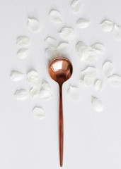 teaspoon on a background of white petals. did table settings, cutlery of copper color.