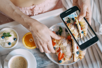 concept breakfast in bed, croissant with strawberries and cream on a light wooden tray with a cup of coffee