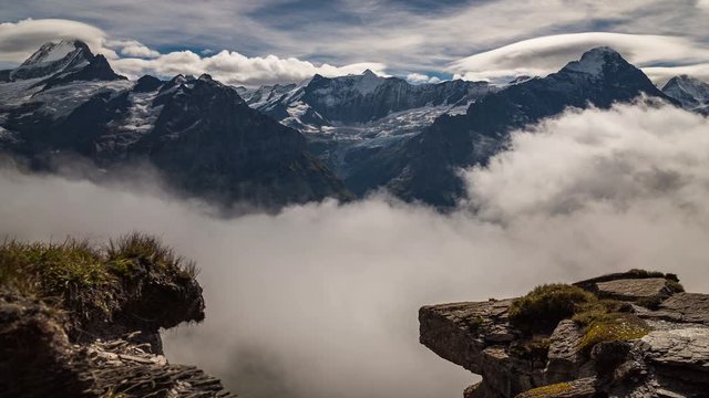 Time lapse of clouds moving over a snowy alpine mountain landscape overlooking a valley below. Captured in the mountains of Grindelwald in Switzerland.