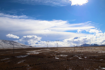 Plateau, high-voltage transmission tower, blue sky and white clouds, ice lake and distant Shishapangma Peak