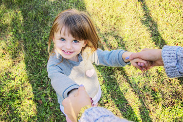 Point of view of young mother holding hands of her little cheerful girl. Tiny child holding hands of her mom and smiling while playing in park. Happy mother and daughter having fun outdoors