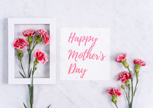 Happy Mother's Day background design concept with greeting words, beautiful pink, red carnation flower bouquet on marble table, top view, flat lay, copy space.