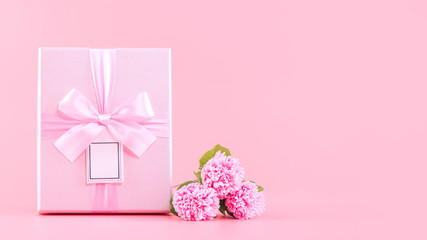 Mother's Day holiday gift design concept, pink carnation flower bouquet with wrapped box isolated on light pink background, copy space.