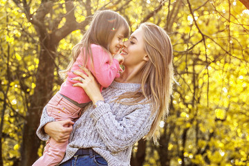 Cheerful young mother holding her little daughter in hands and laughing while having fun in autumn...