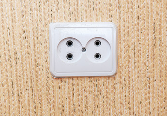 European electric outlet on wall covered with wallpaper