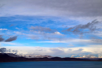 Sunny after the snow, the hut on the pasture, the snowy mountains in the distance, the blue sky and white clouds, the road leading to the distance, the high-voltage power transmission line, the very s