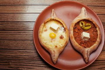 Top view on tasty traditional Adjarian Khachapuri - open baked pie with melted salt cheese suluguni and egg and Khachapuri with meat and pepperyolk on wooden tray. raditional georgian food