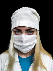 Young female doctor in a protective medical mask, medical cap and dressing gown with her hair down on an isolated black background, an empty space for your design