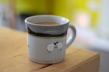 A cup of tea in a mug with sheep on stood on a wooden table 