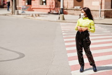 African American woman posing with facial mask to protect from infections from bacteria, viruses and epidemics, standing on pedestrian crosswalk.