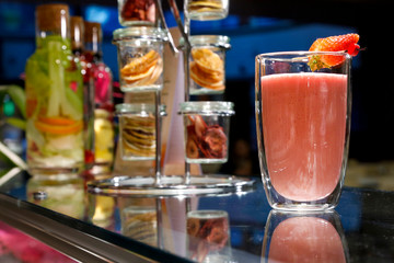 Fototapeta na wymiar Succo di frutta colorato con fragola sul bancone di vetro di un bar e sullo sfondo altri contenitori di vetro con frutta essiccata 