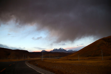 Under the sunset, the snowy mountains in the distance, the brown mountain slopes, and the road to the distance