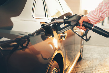 A man’s hand holding petrol pump and refueling his new car with fuel at the refuel station