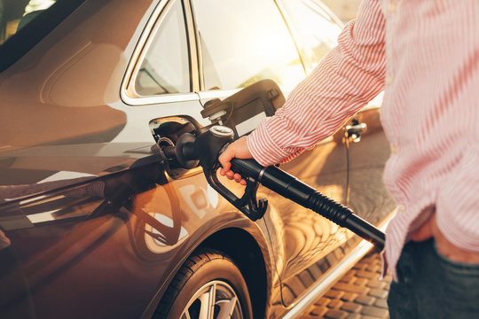 A Man Holding Petrol Pump And Refuelling His New Car With Fuel At The Gas Station. Sunset Lighting